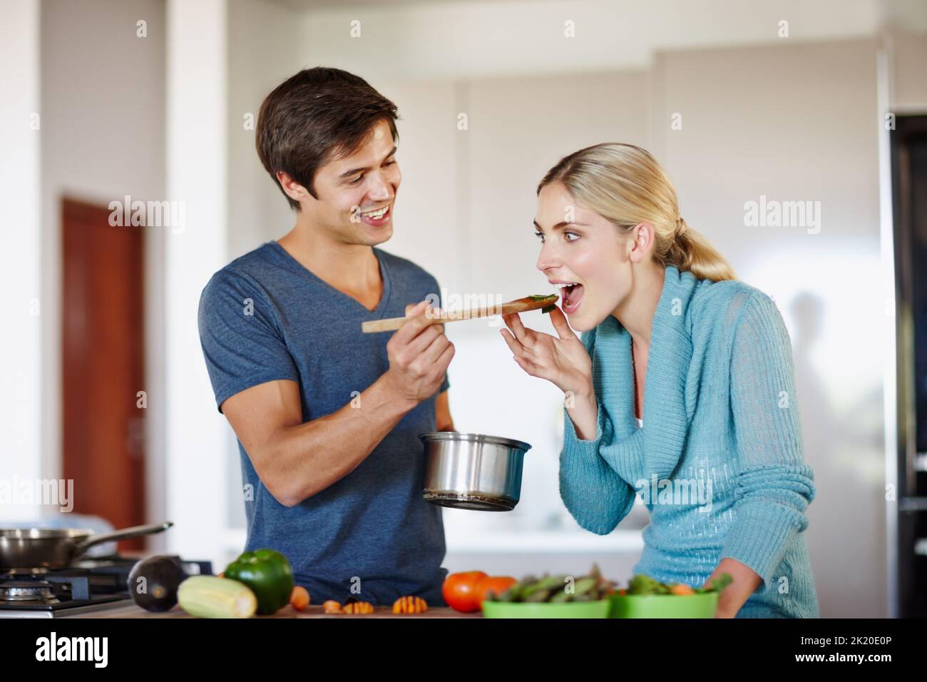 Ich bin sicher, es schmeckt so gut wie es riecht. Ein hübscher junger Mann, der seiner Frau einen Vorgeschmack auf seine Küche gibt. Stockfoto