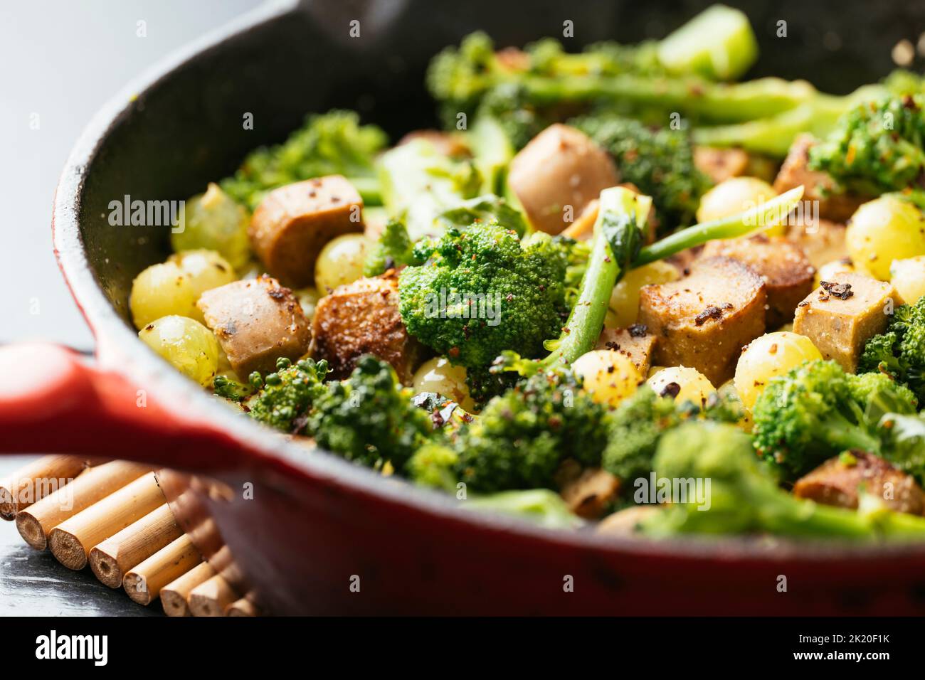 Vegane Wurst mit Broccoli und Trauben in einer gusseisernen Pfanne. Stockfoto
