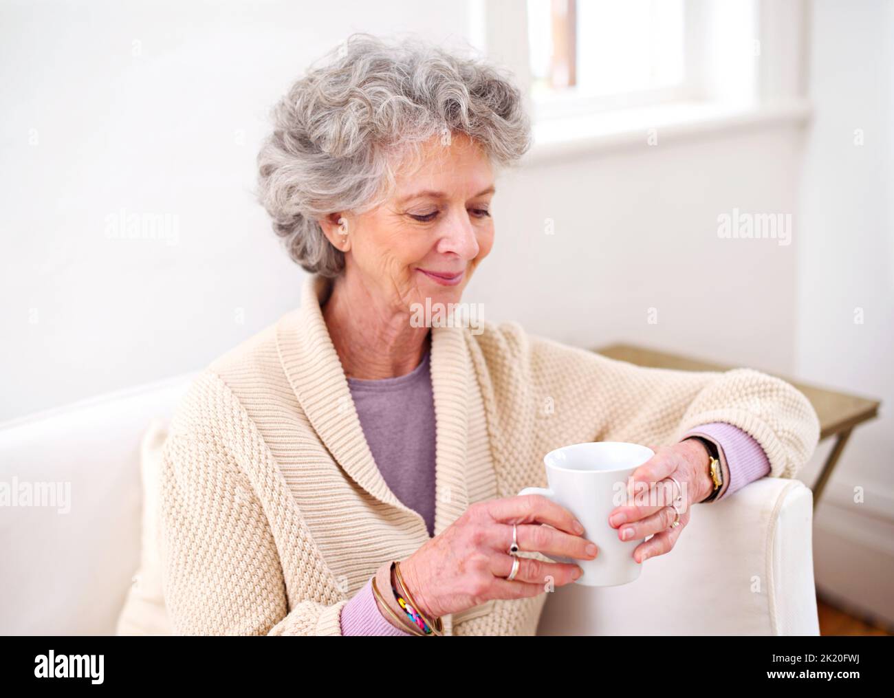 Ich kann mich noch an diesen Tag erinnern... eine ältere Frau, die eine Tasse Kaffee auf dem Sofa hielt. Stockfoto