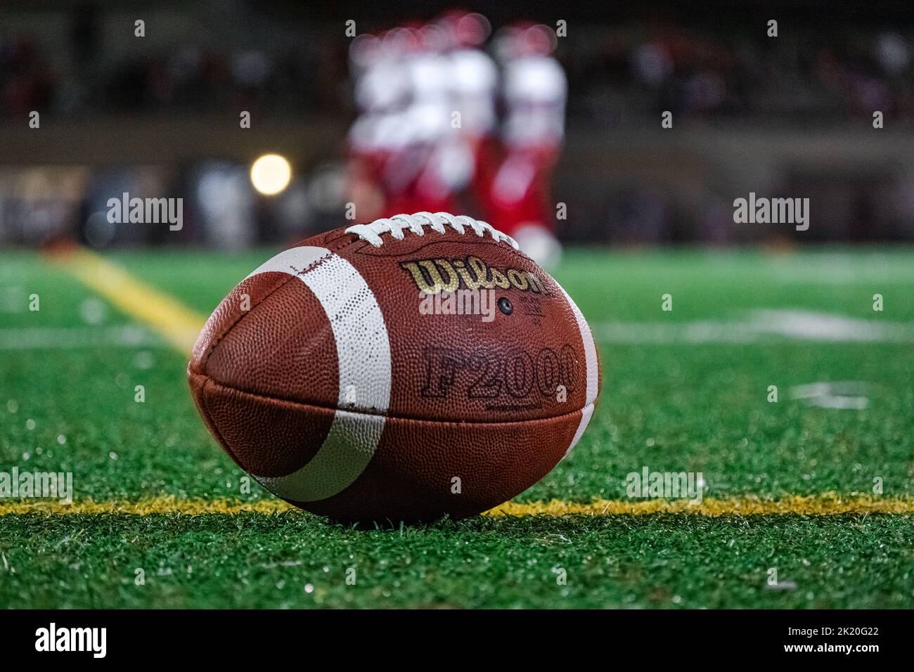 Nahaufnahme eines Wilson Fußballs auf Kunstrasen während eines Nachtfußballspiels mit Spielern im Hintergrund. Stockfoto