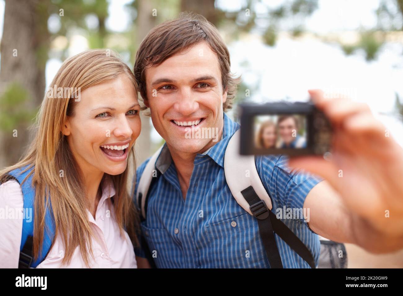 Selbstporträt. Paar mit Rucksack, der auf die Kamera schaut und lächelt, während ein Mann auf ein Foto klickt. Stockfoto