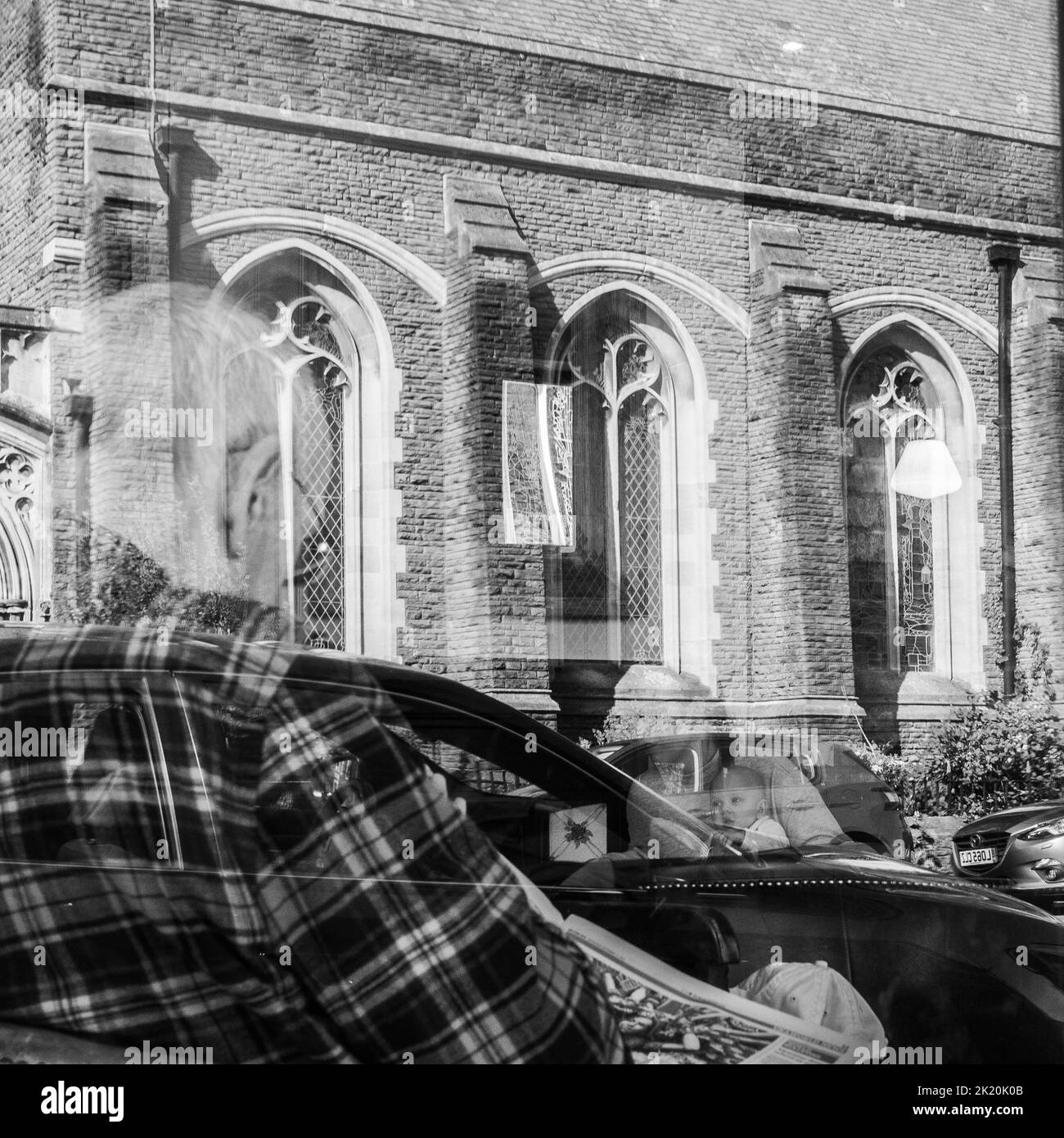 Geisterhaft, abstrakt, Straßenfoto eines alten Mannes, der in einem Café eine Zeitung liest, aufgenommen durch das Café-Fenster Stockfoto