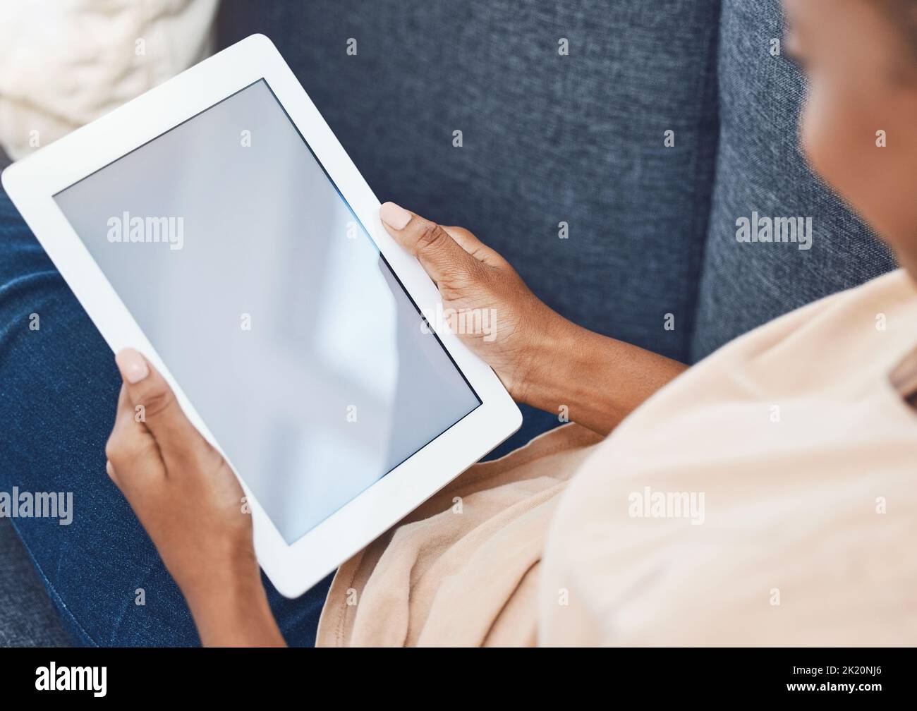 Mockup Digital Tablet, in den Händen einer schwarzen Frau auf der Couch in einem Wohnzimmer in ihrem Haus und geht online, um Unterhaltung zu finden. Es wird mobile Technologie verwendet Stockfoto