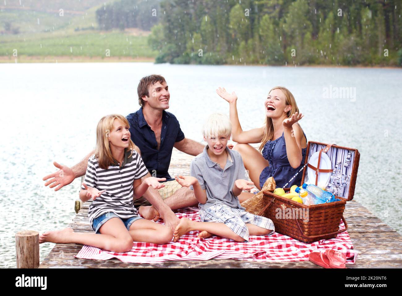 Spaß haben, egal was passiert. Lächelnde junge Familie lacht beim Picknicken, als es zu regnen beginnt. Stockfoto