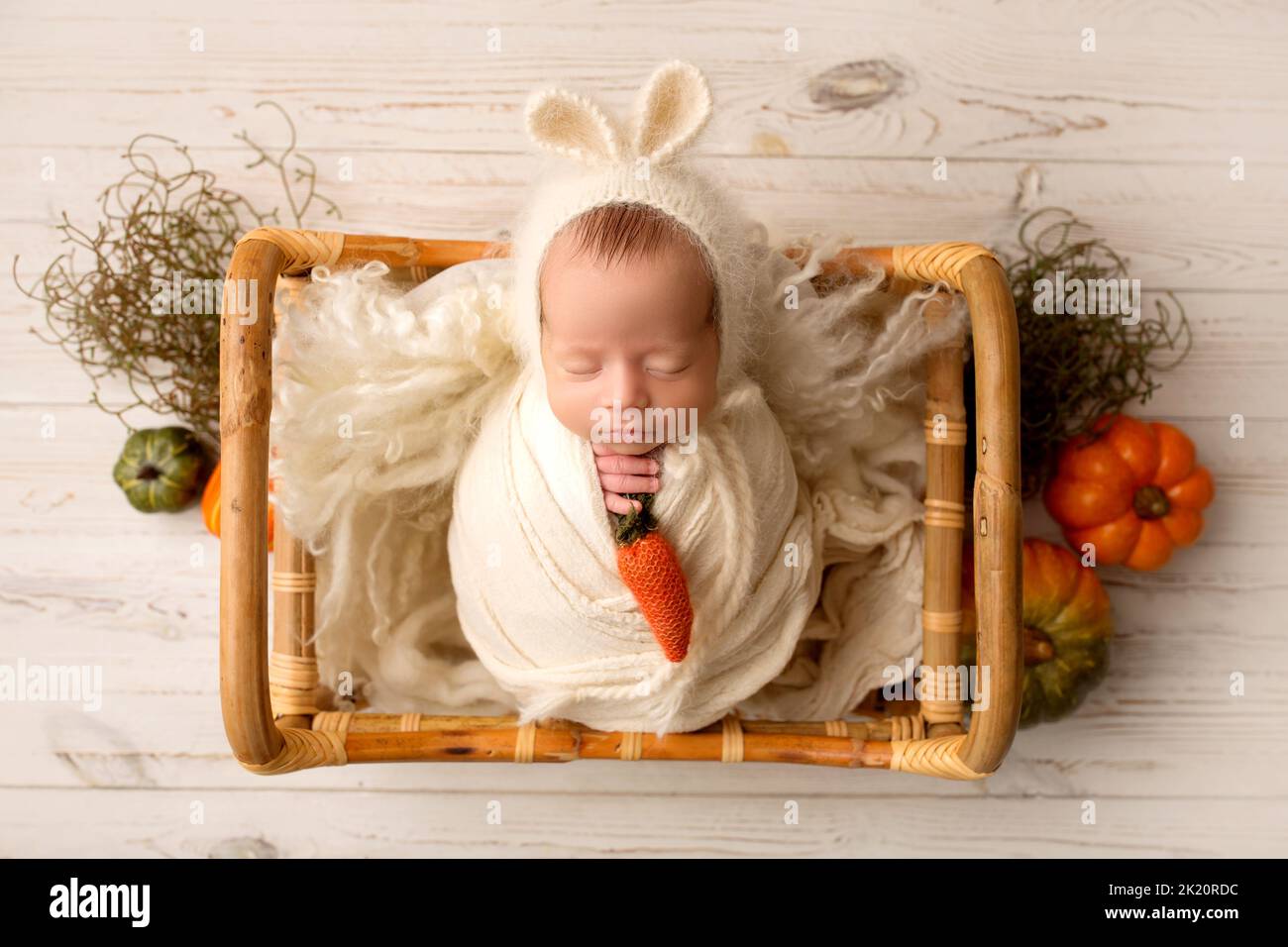 Ein winziger neugeborener Junge in einem weißen Kokon in einem Holzkorb vor einem hellen Holzhintergrund. Hasenhut mit Ohren. Stockfoto