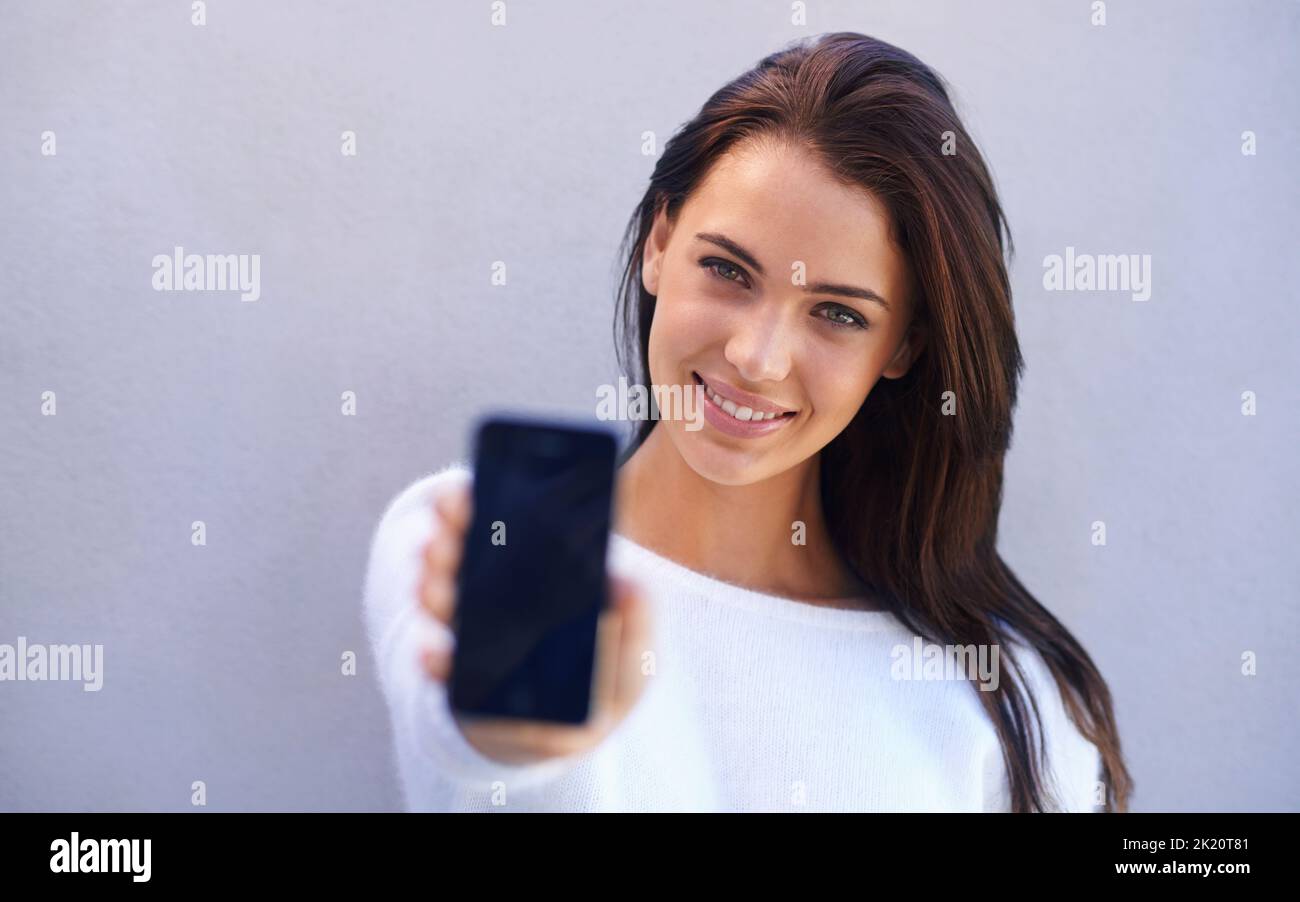 Mit diesem Telefon erhalten Sie auch ein Upgrade für Ihr Leben. Porträt einer attraktiven jungen Frau, die vor einem grauen Hintergrund steht und sie hochhält Stockfoto