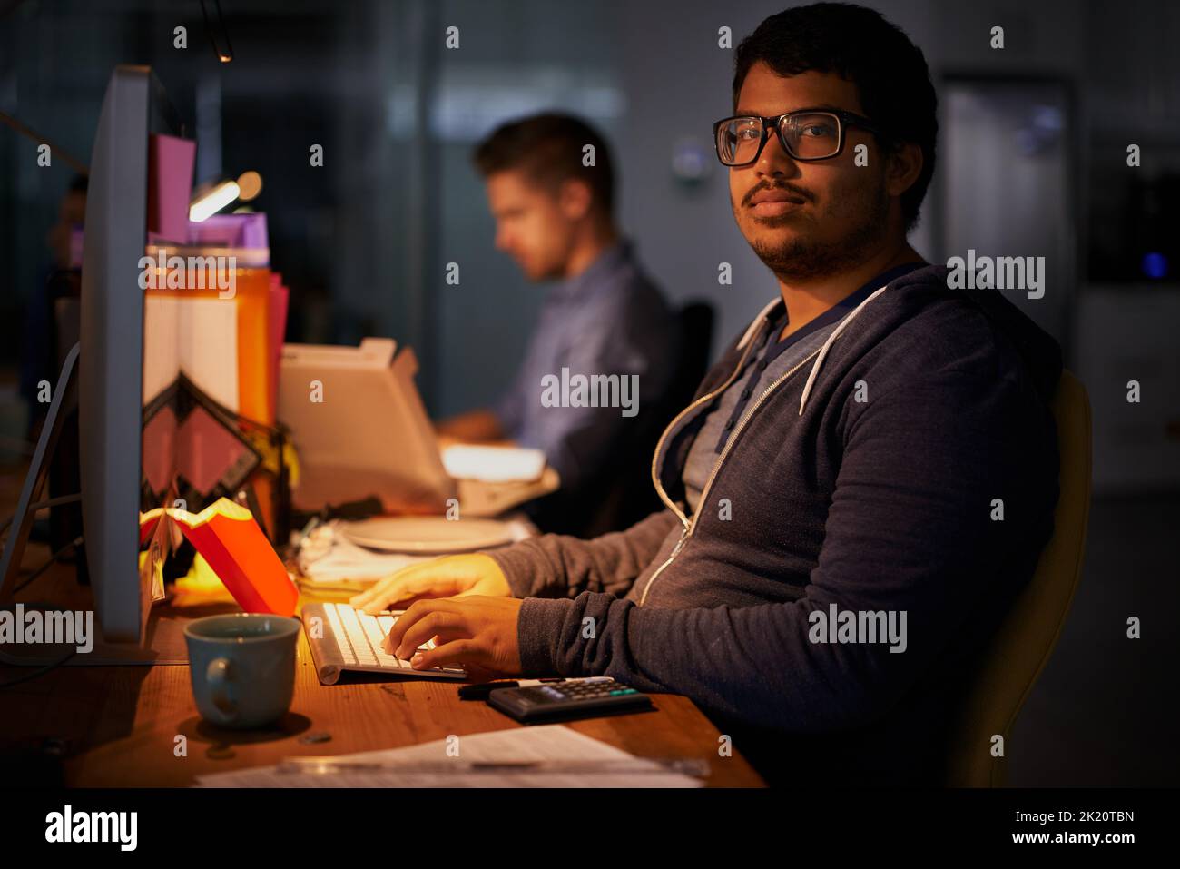 Eine Gruppe junger Mitarbeiter, die in einem schwach beleuchteten Büro arbeiten. Stockfoto
