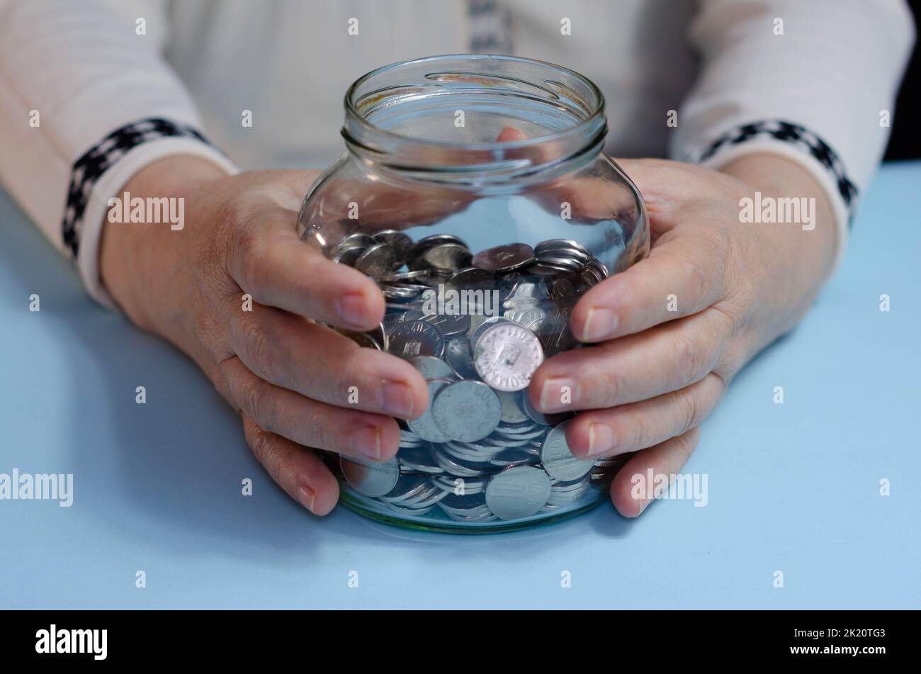 Hände einer älteren Frau mit Geld ron auf der Brieftasche auf blauem Hintergrund. Konzept der Armut im Ruhestand Stockfoto