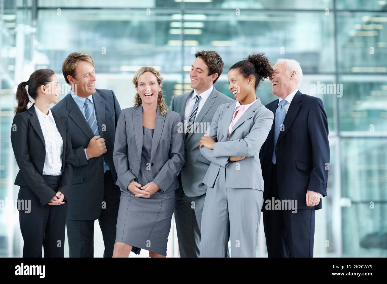 Shes definitiv der Mitarbeiter des Monats. Fröhliche Gruppe von Geschäftsleuten, die zusammen stehen und lächeln, während sie einen Kollegen umzingelnd umzingelnd - Porträt. Stockfoto