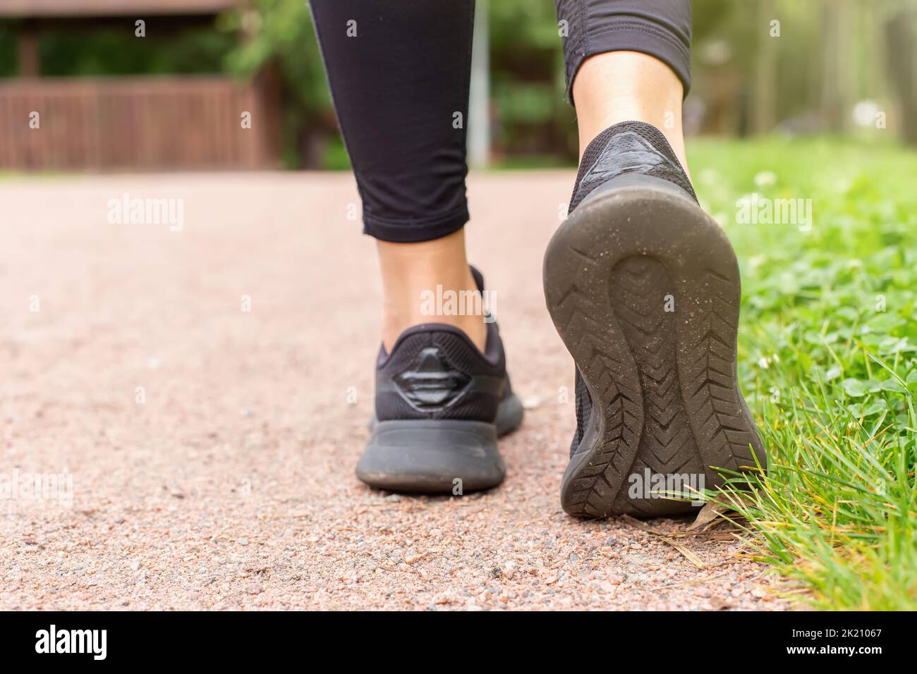 Nahaufnahme der Beine einer Frau, in schwarzen Turnschuhen, auf einem Pfad aus kleinem roten Stein Stockfoto
