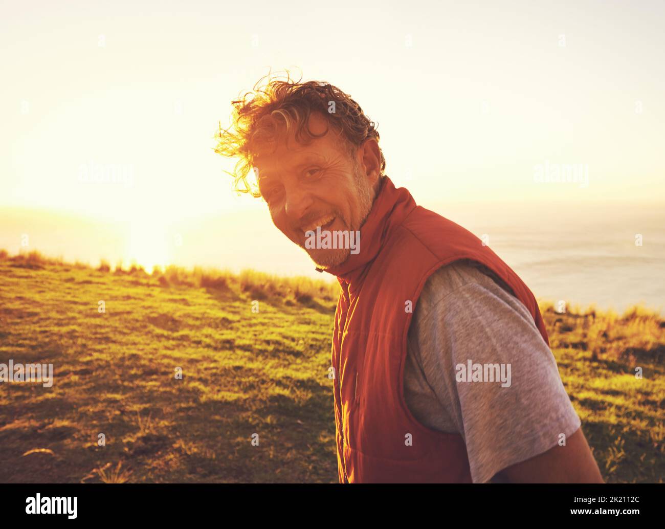 Ich liebe die Zeit weg von der Stadt. Porträt eines Mannes, der bei Sonnenuntergang auf einem Hügel steht, mit dem Ozean im Hintergrund. Stockfoto