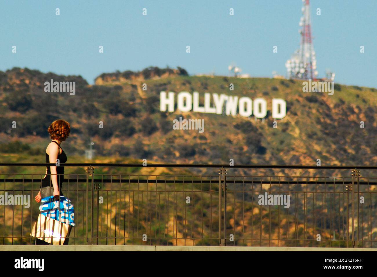 Eine junge Frau trägt ihre Einkaufstasche auf den oberen Etagen des Hollywood- und Highland-Einkaufszentrums und passiert vor dem berühmten Hollywood-Schild Stockfoto