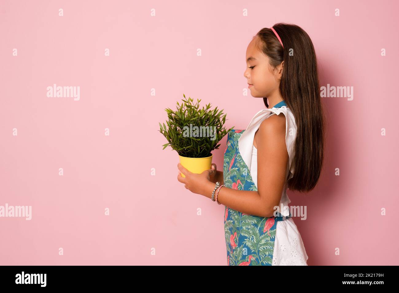 Seitenansicht eines kleinen Mädchens, das eine Pflanze auf einem rosa Hintergrund hält. Stockfoto