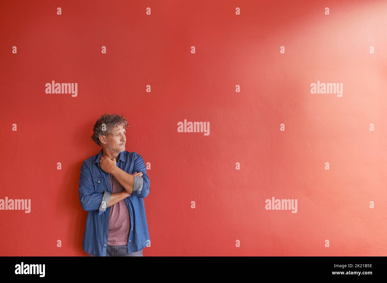 Manchmal muss man einfach nur aufhören und nachdenken. Ein reifer Mann, der vor einem roten Hintergrund steht. Stockfoto