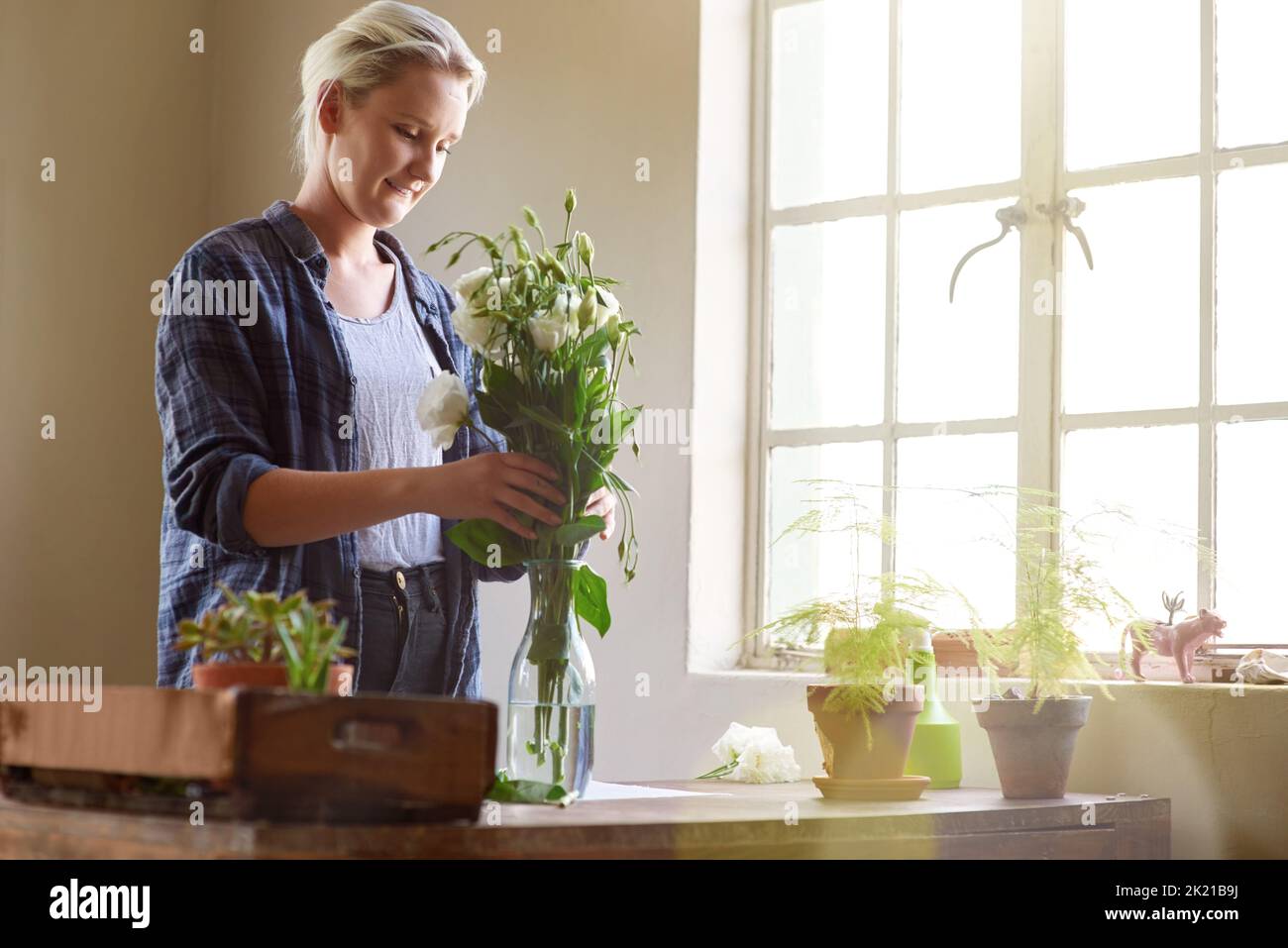 Mal sehen, was wir damit machen können. Ein junger Blumenhändler, der Blumen in einer Vase arrangiert. Stockfoto