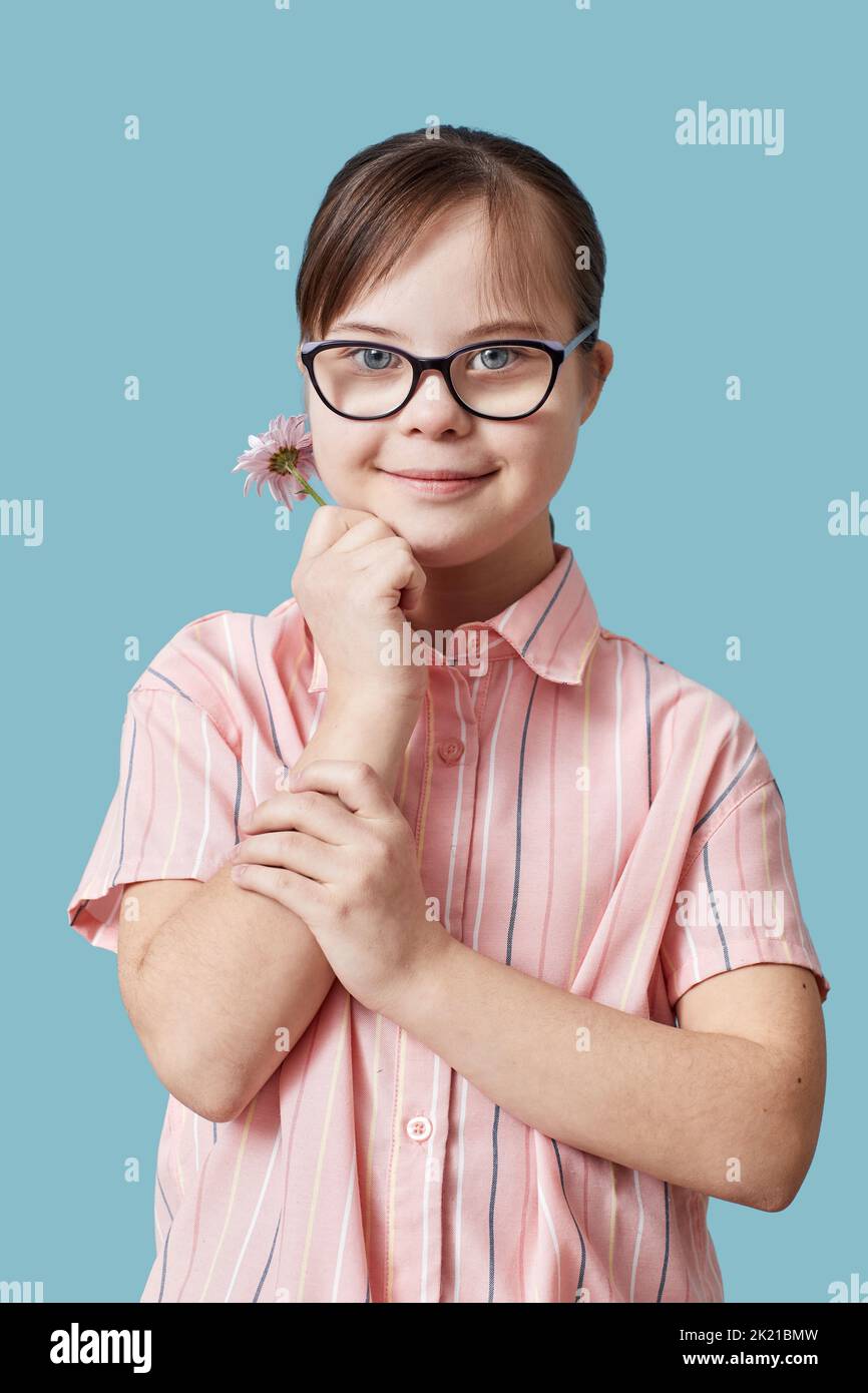 Vertikales Porträt von niedlichen Mädchen mit Down-Syndrom hält Blume vor blauem Hintergrund im Studio Stockfoto
