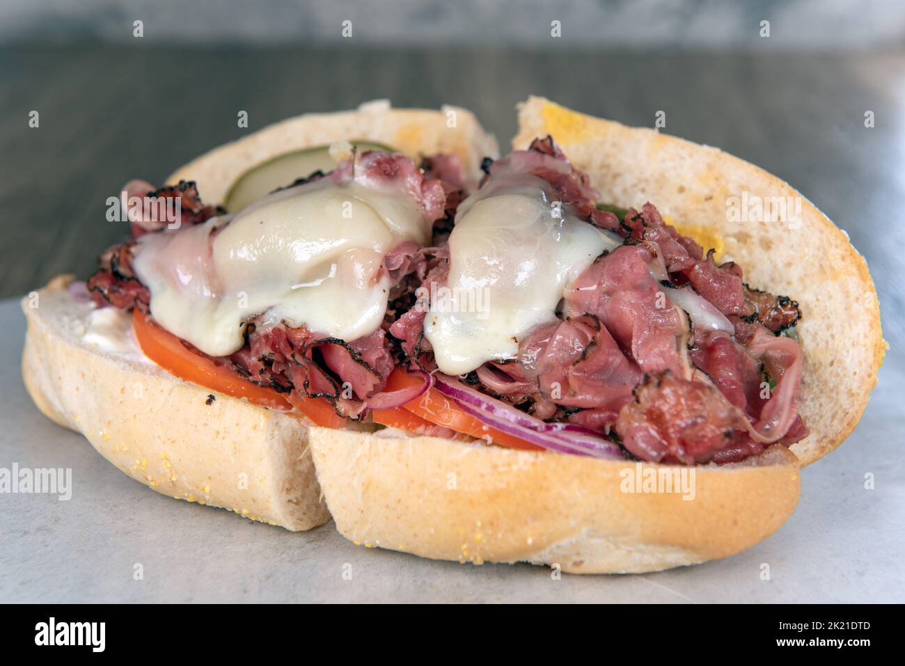 Das Mittagessen wird mit einem beladenen Pastrami-Sub-Sandwich serviert, das mit geschmolzenem Käse überfüllt ist. Stockfoto