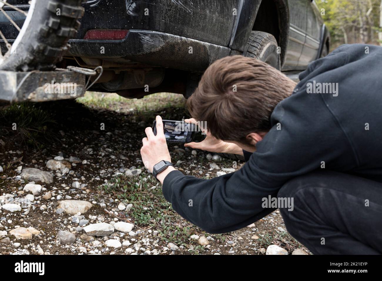 Mann mit Smartphone, der das Fahrwerk eines Overland-SUV fotografiert Stockfoto