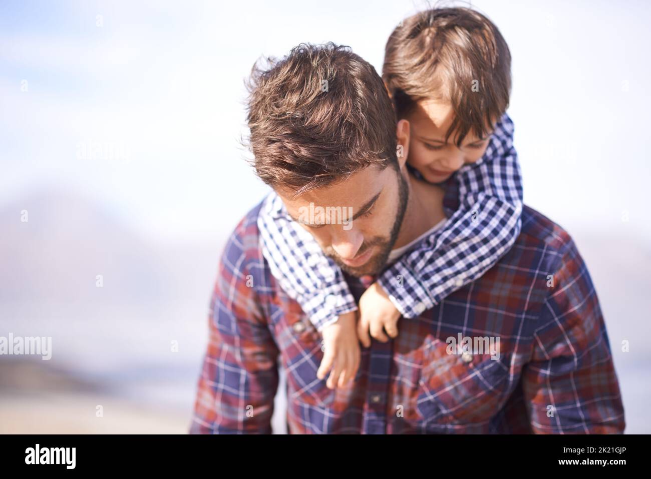 Egal, welcher Vater, du bist mein Held. Ein Vater, der seinen kleinen Sohn auf dem Rücken trägt, während er nach unten blickt. Stockfoto