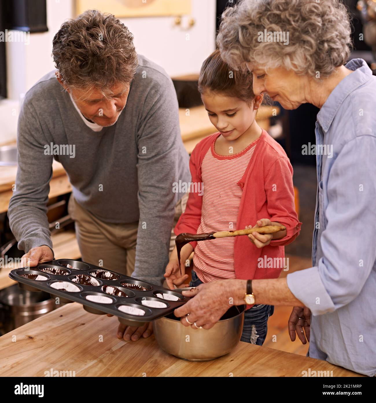 Nur noch ein paar weitere... ein kleines Mädchen und ihre Großeltern machen Cupcakes in der Küche. Stockfoto