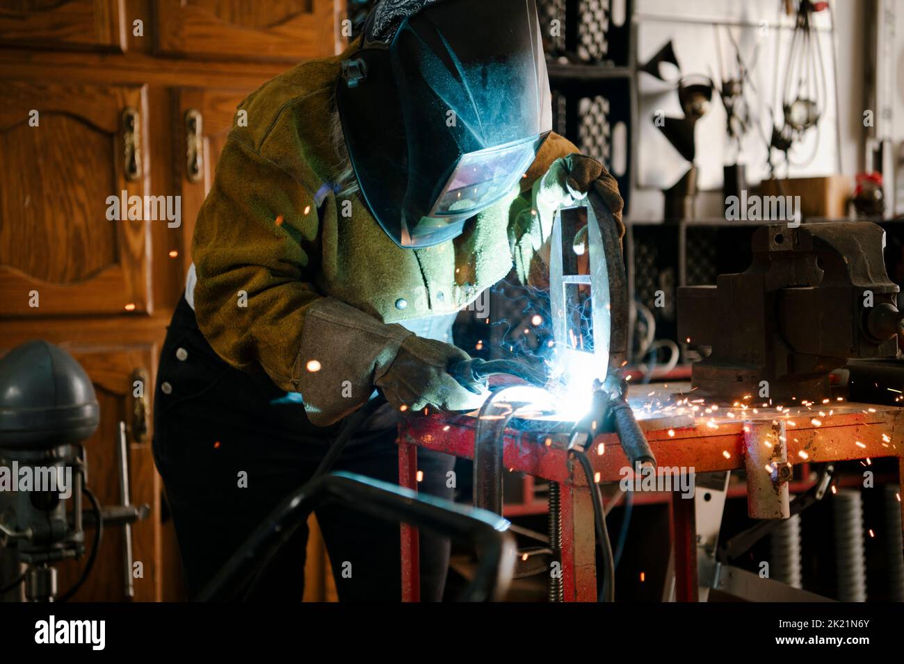 Bildhauerin in Schweißmaske mit Schweißbrenner in der Werkstatt Stockfoto