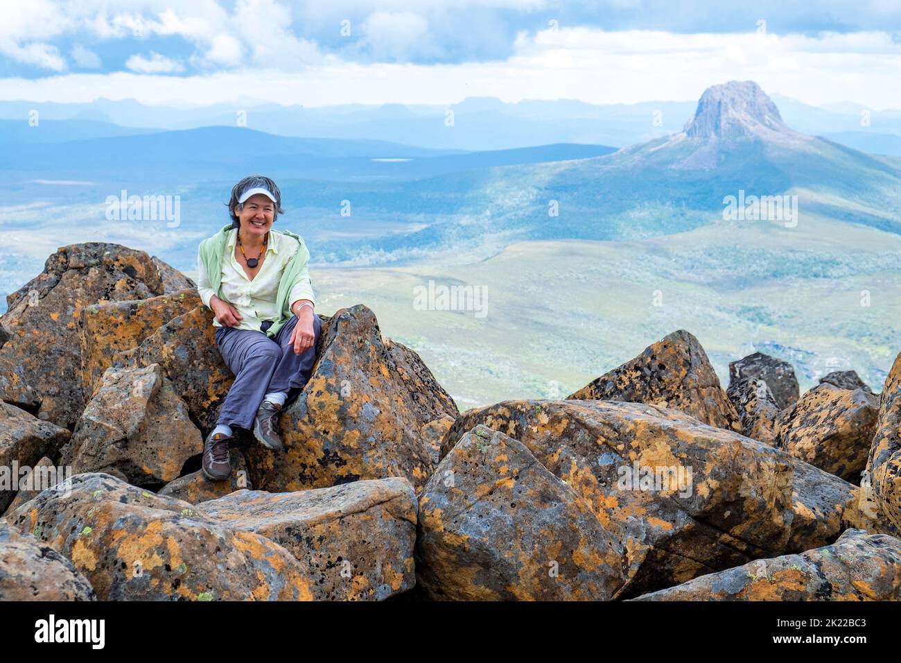 Reife Frau auf dem Gipfel des Cradle Mountain in Tasmanien mit geologischer Besonderheit Barn Bluff im Hintergrund Stockfoto