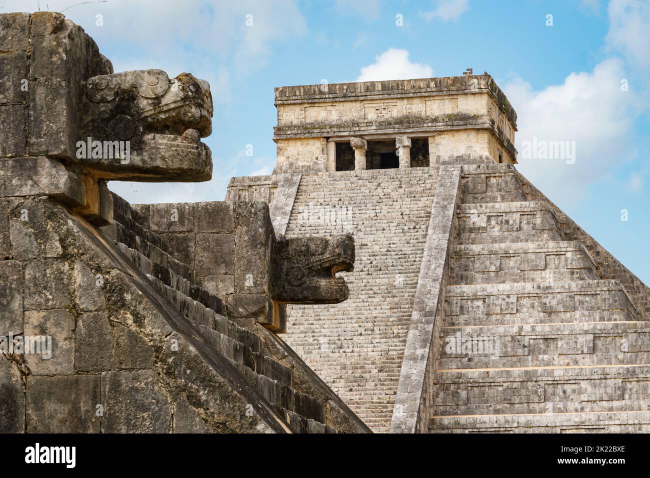 Blick auf El Castillo (Tempel von Kukulkan) hinter geschnitzten jaguar Köpfen. Blauer Himmel und Wolken im Hintergrund. Stockfoto