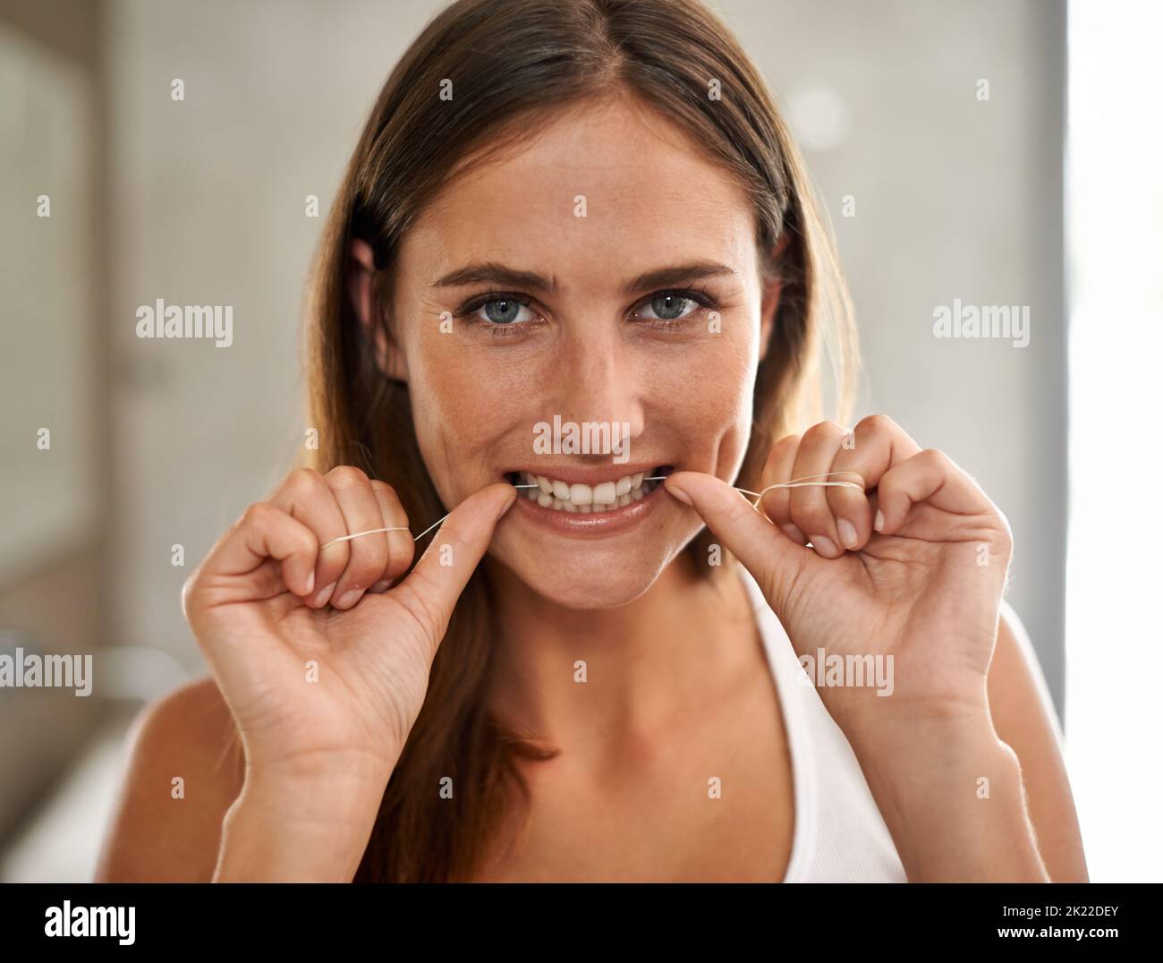 Meine Schönheit beginnt mit einem strahlenden Lächeln. Porträt einer jungen Frau, die ihre Zähne in einem Badezimmer mit Zahnseide verputzt. Stockfoto