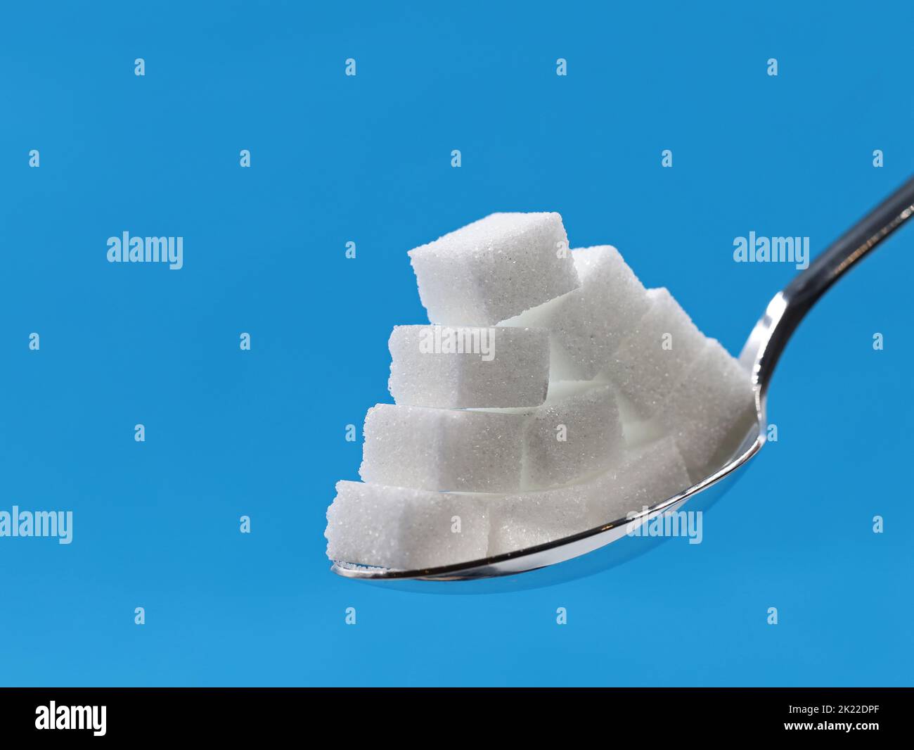 Zuckerwürfel Pyramide auf silbernem Löffel isoliert auf blauem Hintergrund mit Kopierraum Stockfoto