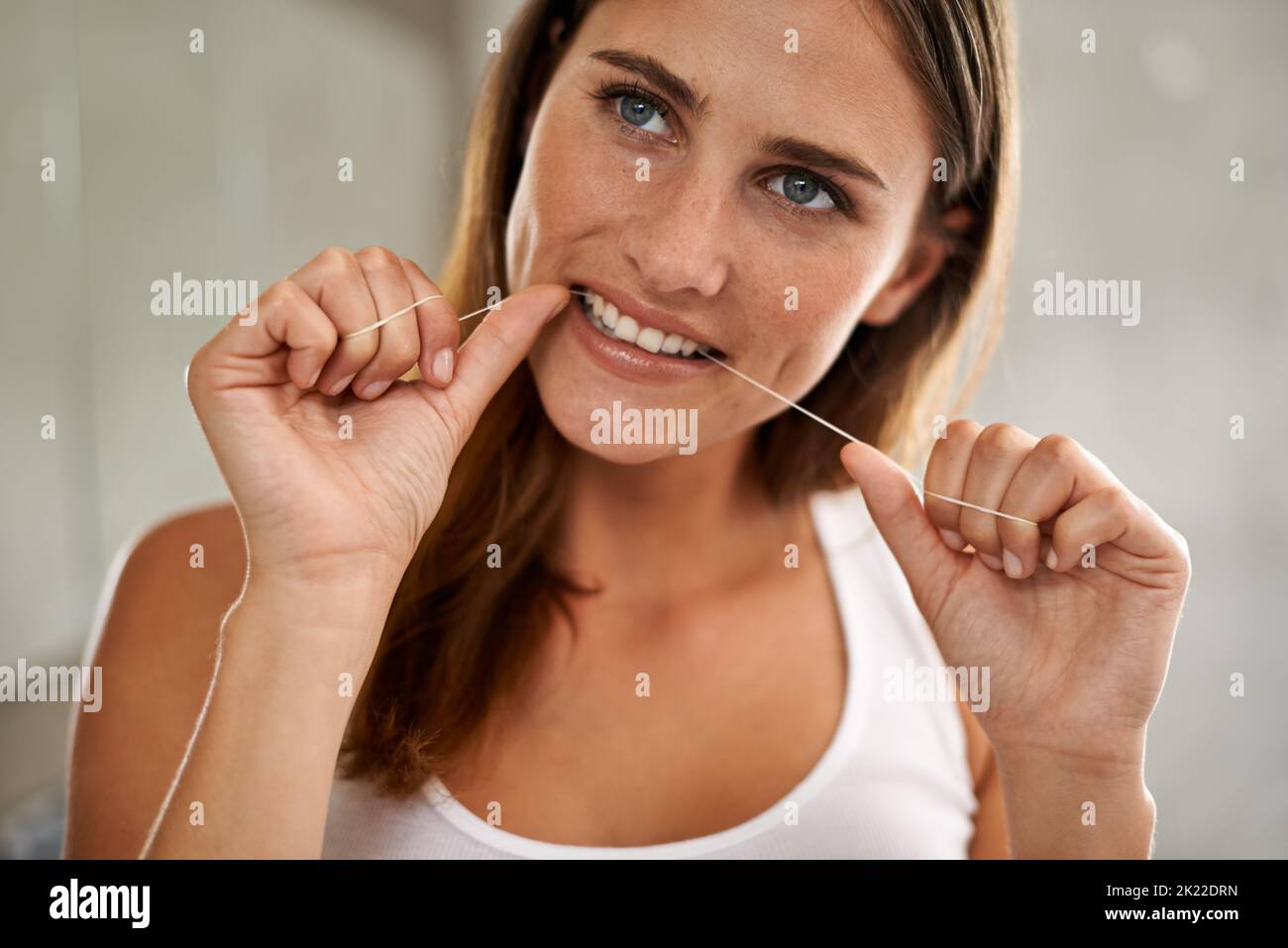 Meine Zähne werden wunderschön sein. Eine junge Frau, die ihre Zähne in einem Badezimmer mit Zahnseide ausgibt. Stockfoto