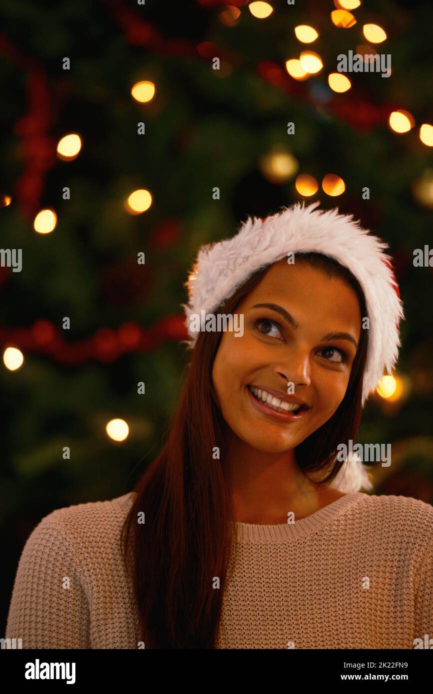 Denken Sie an alle Geschenke. Eine attraktive ethnische Frau, die vor einem weihnachtsbaum denkt. Stockfoto