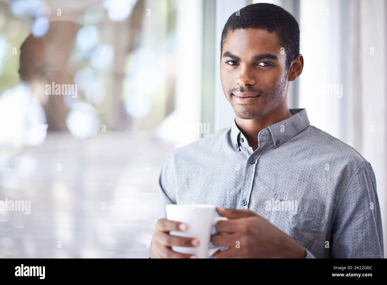 Es ist ein nagelneuer Tag. Porträt eines hübschen jungen Mannes, der eine Tasse Kaffee in der Hand hält, während er am Fenster steht. Stockfoto