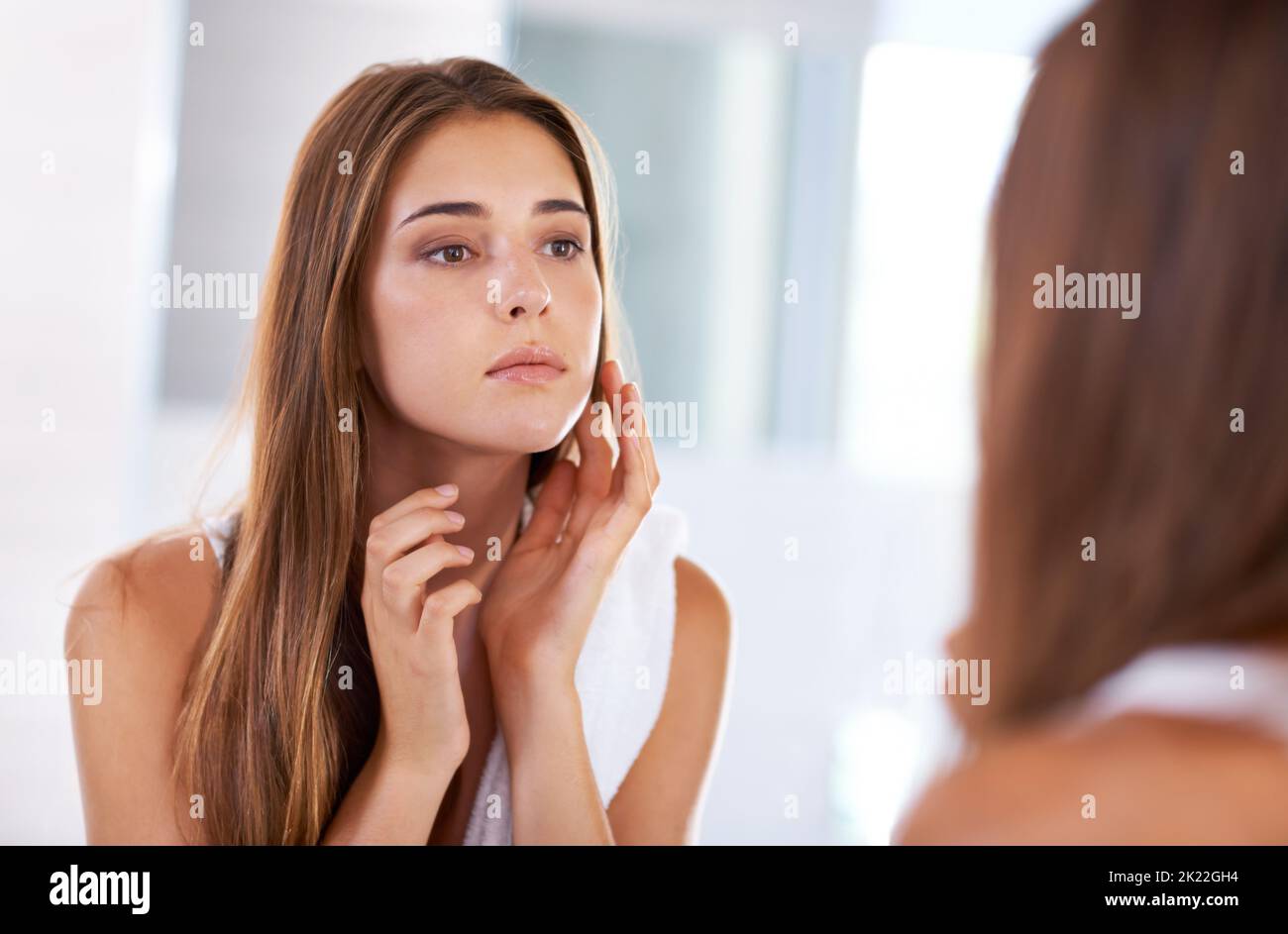 Schönheit beurteilen. Über die Schulter einer attraktiven jungen Frau, die ihre Spiegelung in einem Spiegel betrachtet. Stockfoto