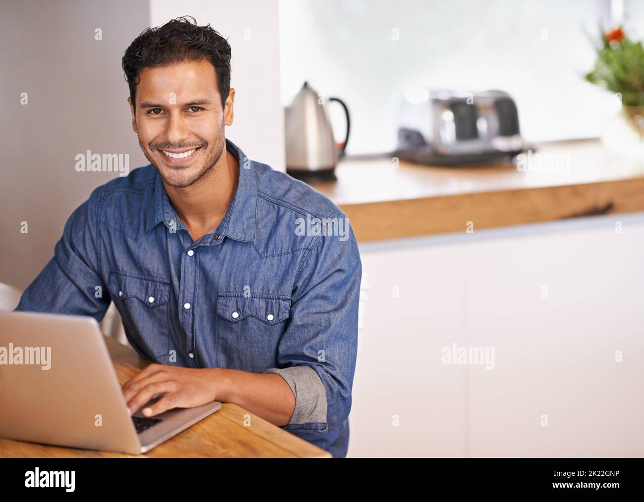 Treffen mit Freunden. Porträt eines hübschen Mannes, der in der Küche an seinem Laptop arbeitet. Stockfoto