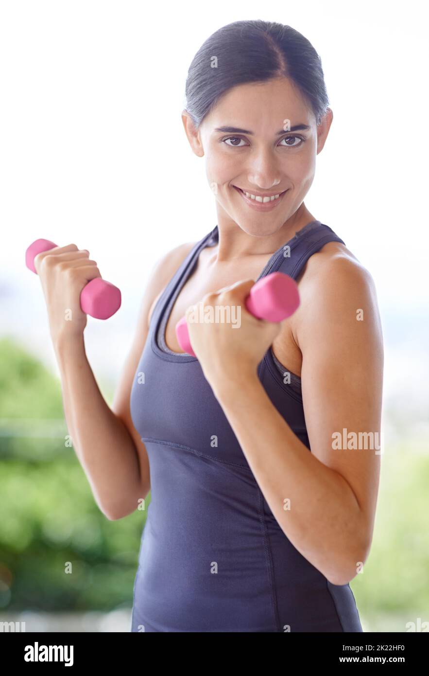 Eine junge Frau lächelt an der Kamera, während sie mit Gewichten arbeitet. Stockfoto