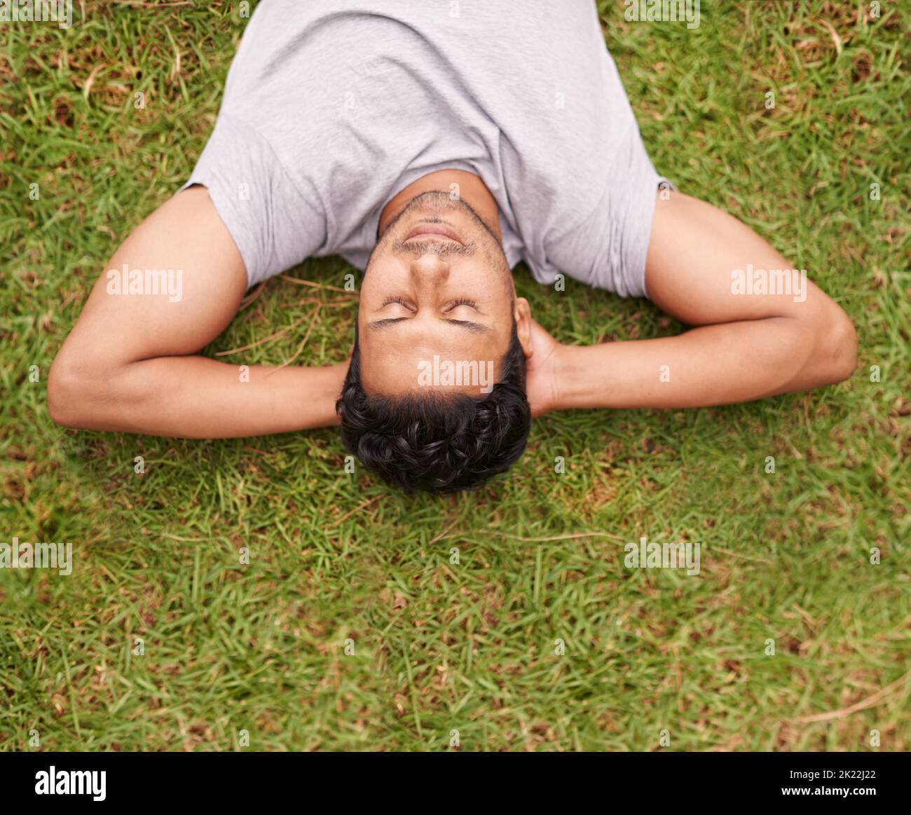 Sich Zeit nehmen, um sich zu entspannen. Ein junger Mann, der auf dem Gras liegt, mit den Händen hinter dem Kopf. Stockfoto