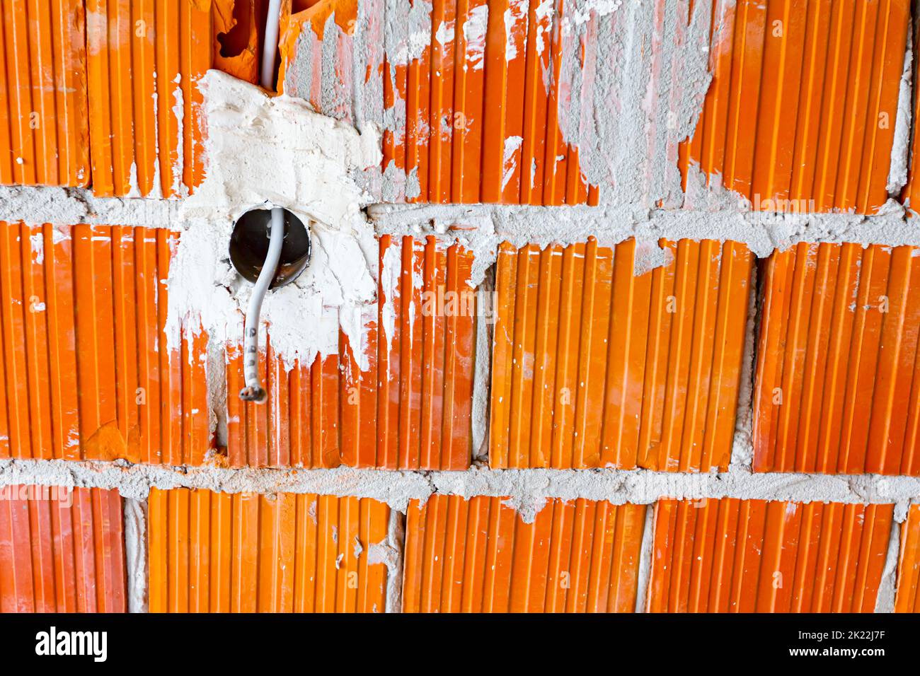 Eine freiliegende Steckdose mit entfernter oberer Abdeckung für die Installation der Verkabelung an der Wand mit im Bau befindlichen Gebäudeblöcken. Stockfoto