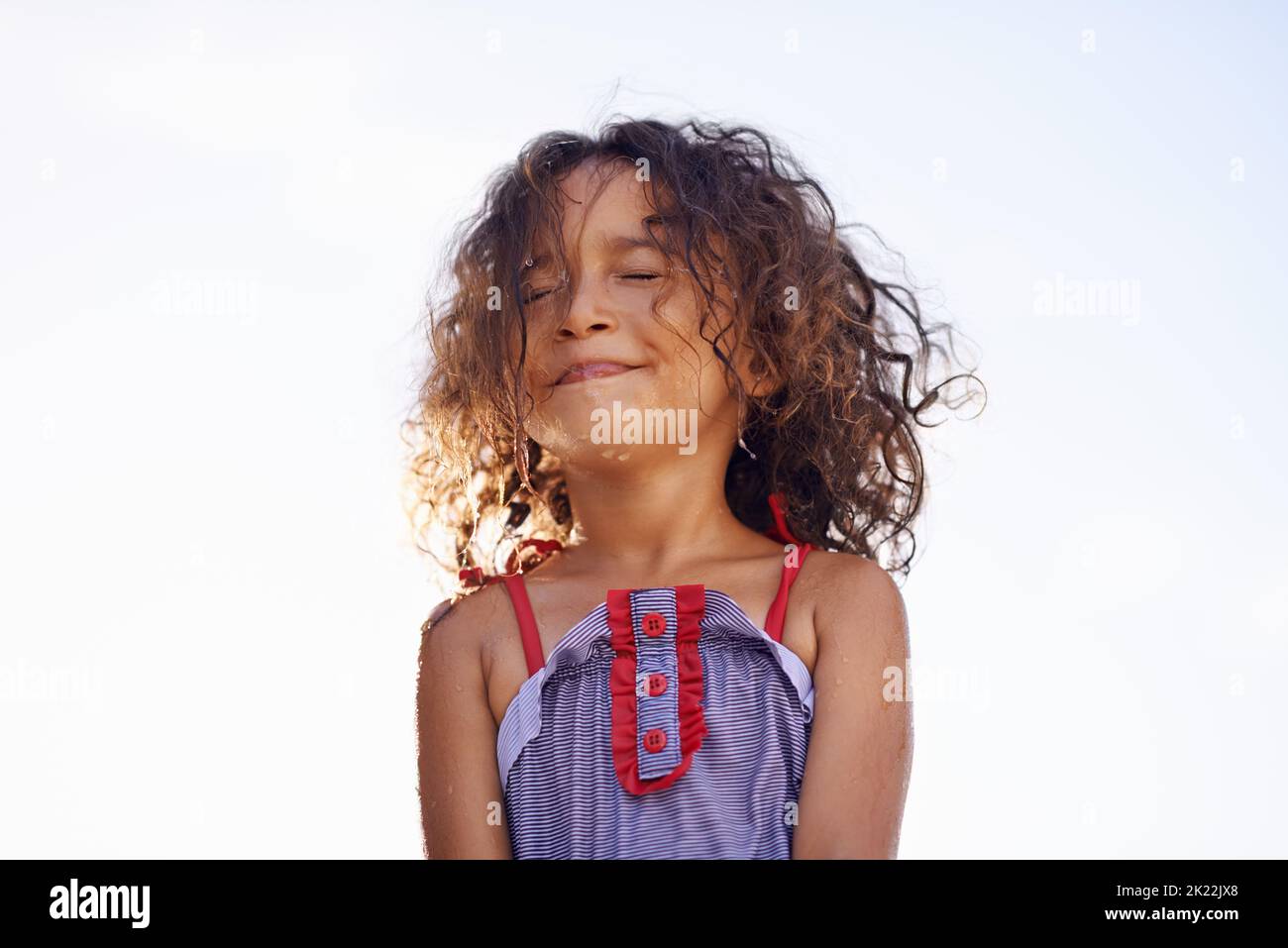 Genießen Sie die Sonne. Ein kleines Mädchen in einem Kostüm mit Wasser spritzte auf ihr Gesicht. Stockfoto
