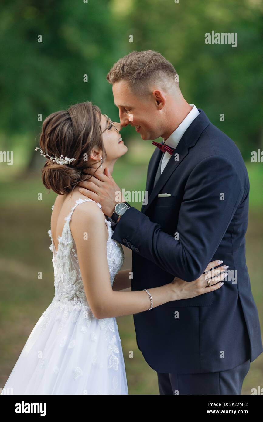 Junger Mann Bräutigam legte die Arme um den Hals der jungen schönen Frau Braut, umarmt, Augen treffen, küssen. Feiern. Stockfoto