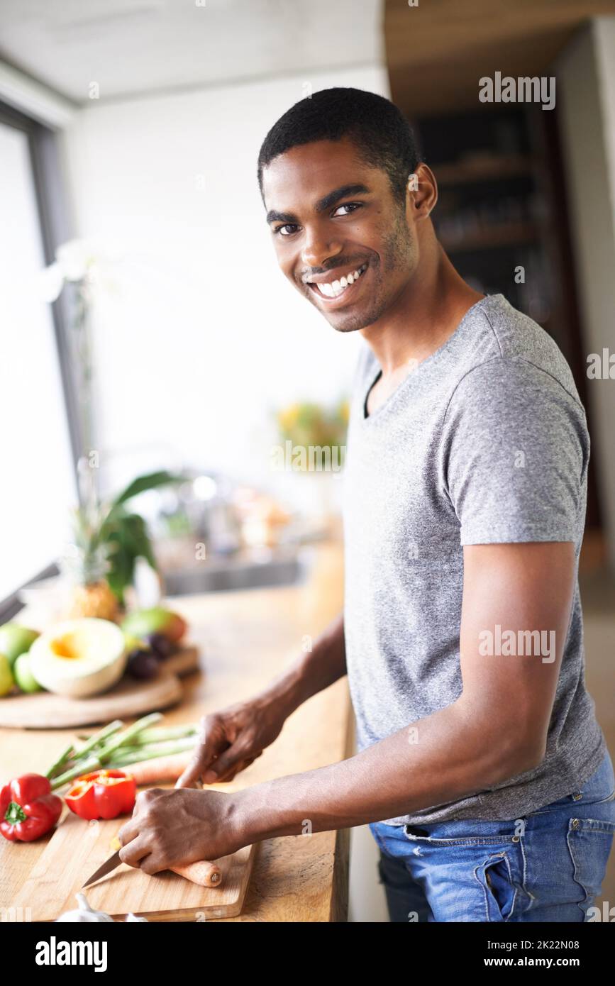 Hes ein glücklicher Herd. Ein gutaussehender ethnischer Mann, der Gemüse im Haus zubereitet. Stockfoto