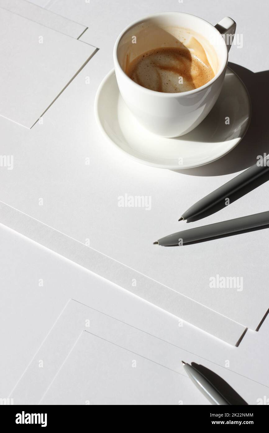 Minimaler Workplace Flatlay. Leere Papierblätter, Stifte, Schreibwaren, Tasse Kaffee auf weißem Hintergrund. Business Mockup. Stockfoto