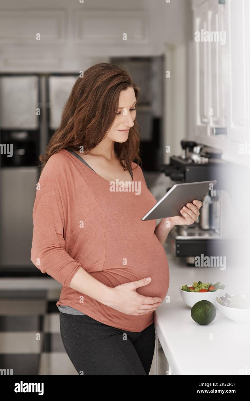 Aufpassen, was sie isst. Eine Schwangerin benutzt ihr Tablet in der Küche. Stockfoto