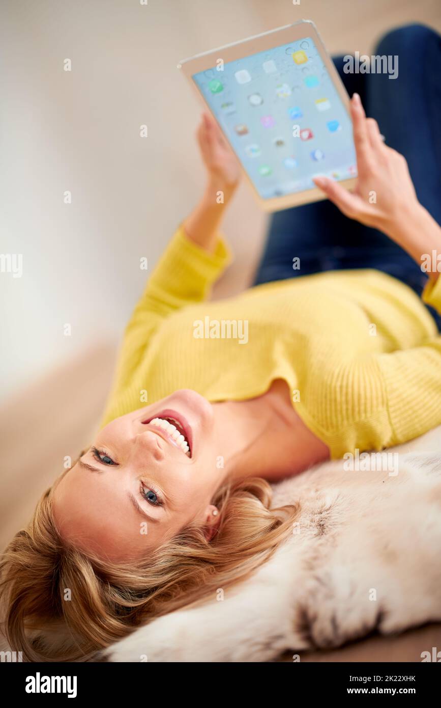 Schließlich fand sie eine Tablette, die gut für ihre Gesundheit war. Eine junge Frau, die glücklich lacht, während sie auf dem Boden liegt und ein digitales Tablet hält. Stockfoto