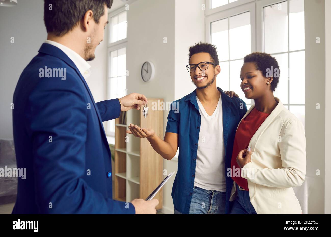 Während des Treffens mit glücklichen jungen verheirateten Paar realtor gibt ihnen Schlüssel zu ihrem neuen Zuhause. Stockfoto