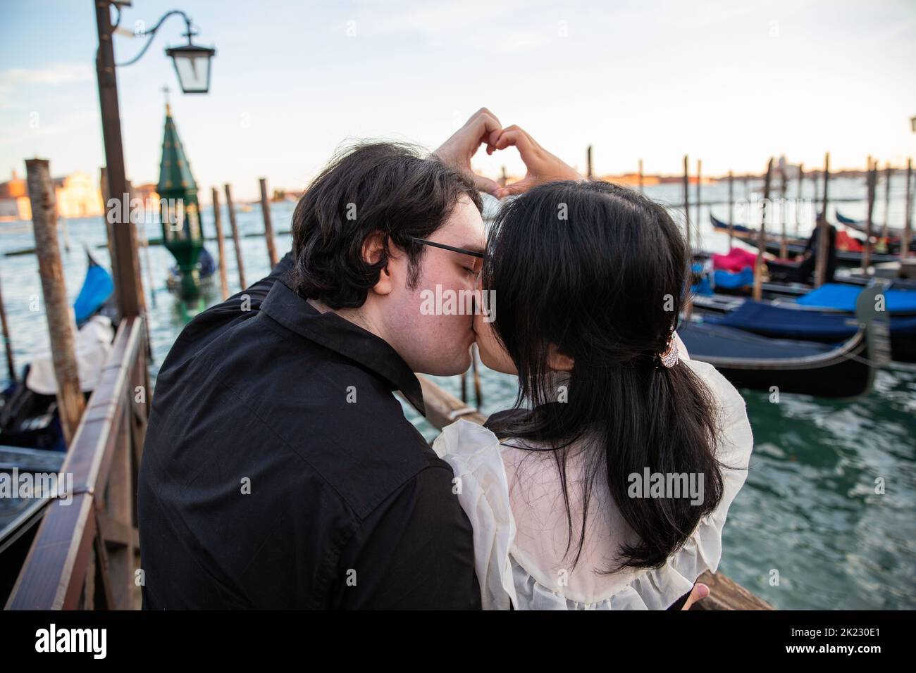 Ein paar Liebende küssen in Venedig während des Sonnenuntergangs und sie machen ein Herz mit ihren Händen, ein romantischer Moment Stockfoto