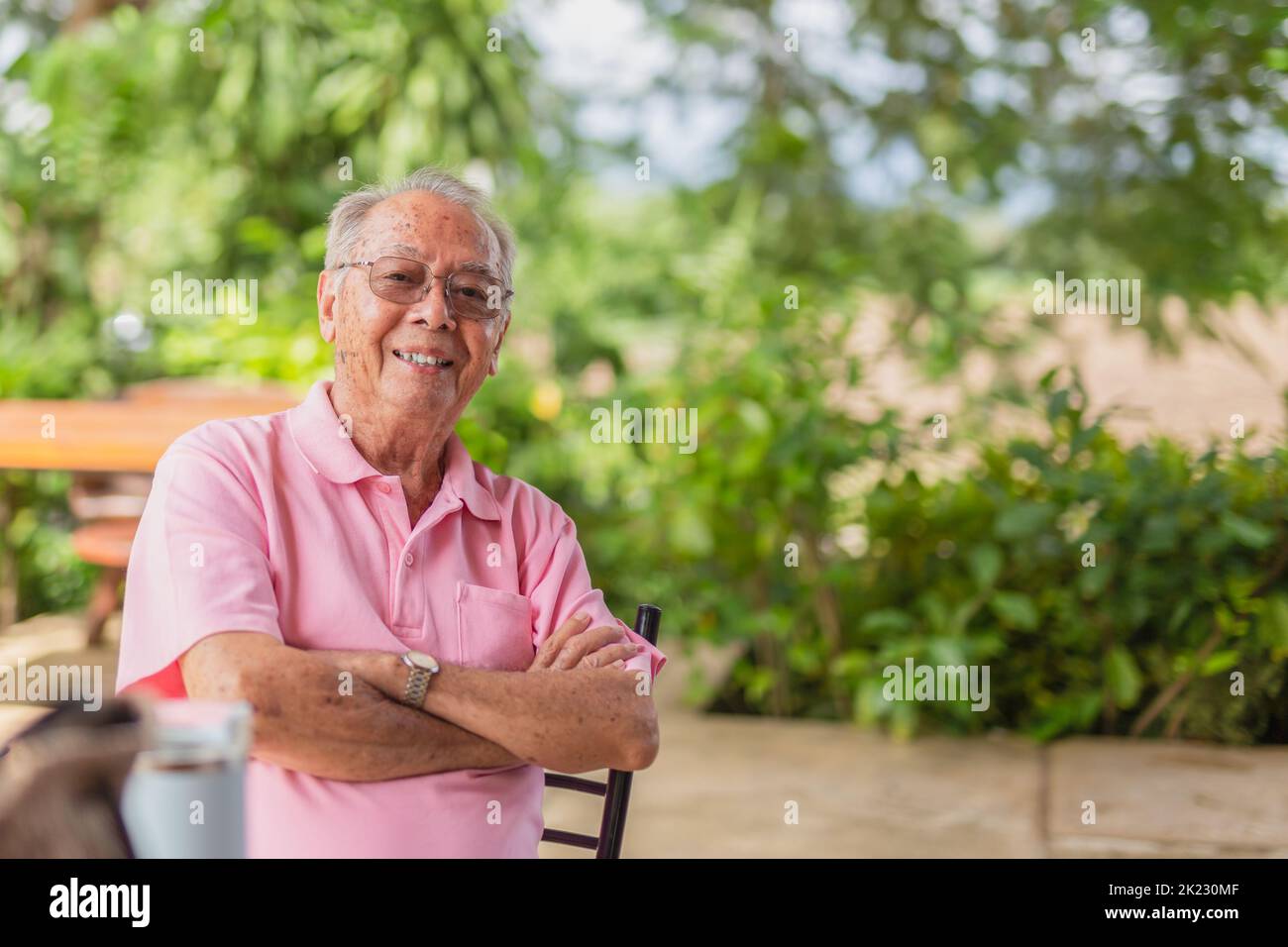 Porträt Asian älterer Mann 83 Jahre alt mit toothy Lächeln sitzen im Freien im Garten. Stockfoto