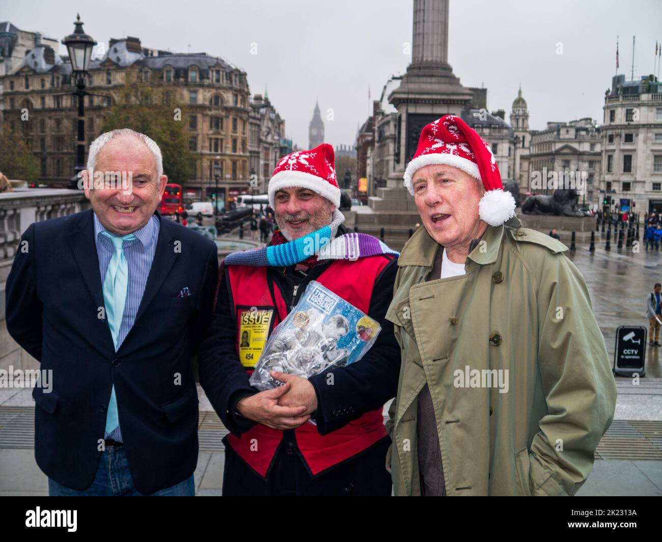Big Issue Gründer John Bird, ein Big Issue Verkäufer und Schauspieler Christopher Timothy bei einer Weihnachtsfeier am Trafalgar Square, London, Großbritannien Stockfoto