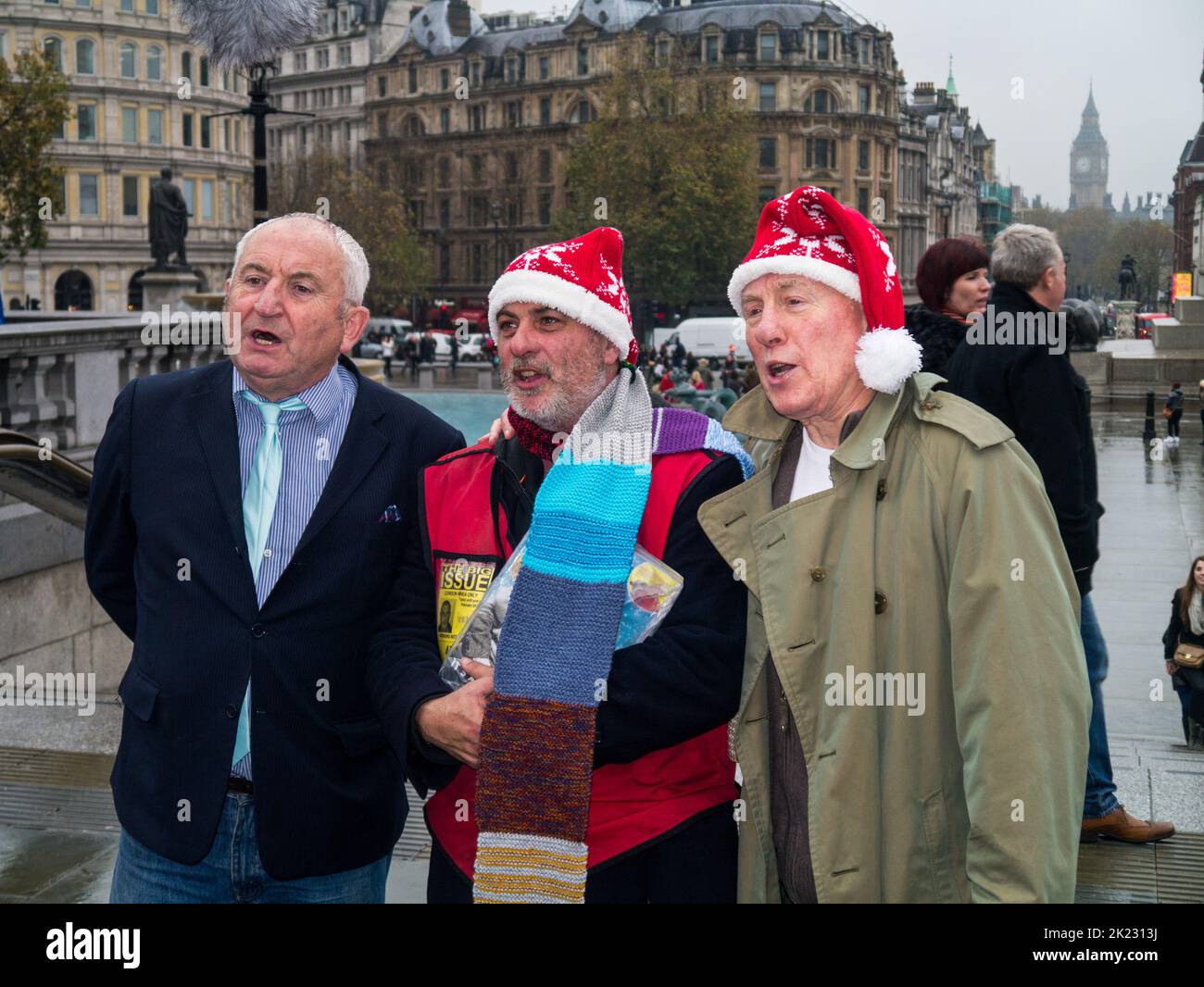 Big Issue Gründer John Bird, ein Big Issue Verkäufer und Schauspieler Christopher Timothy bei einer Weihnachtsfeier am Trafalgar Square, London, Großbritannien Stockfoto