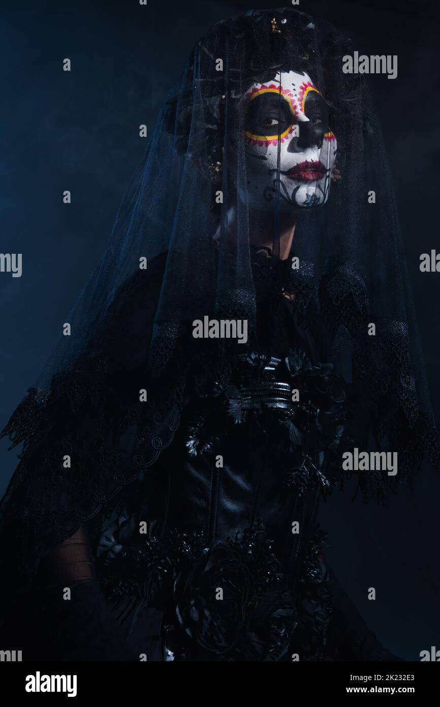Frau in traditionellen santa muerte Make-up und schwarze Spitze Schleier Blick auf die Kamera auf dunkelblauem Hintergrund, Stockbild Stockfoto