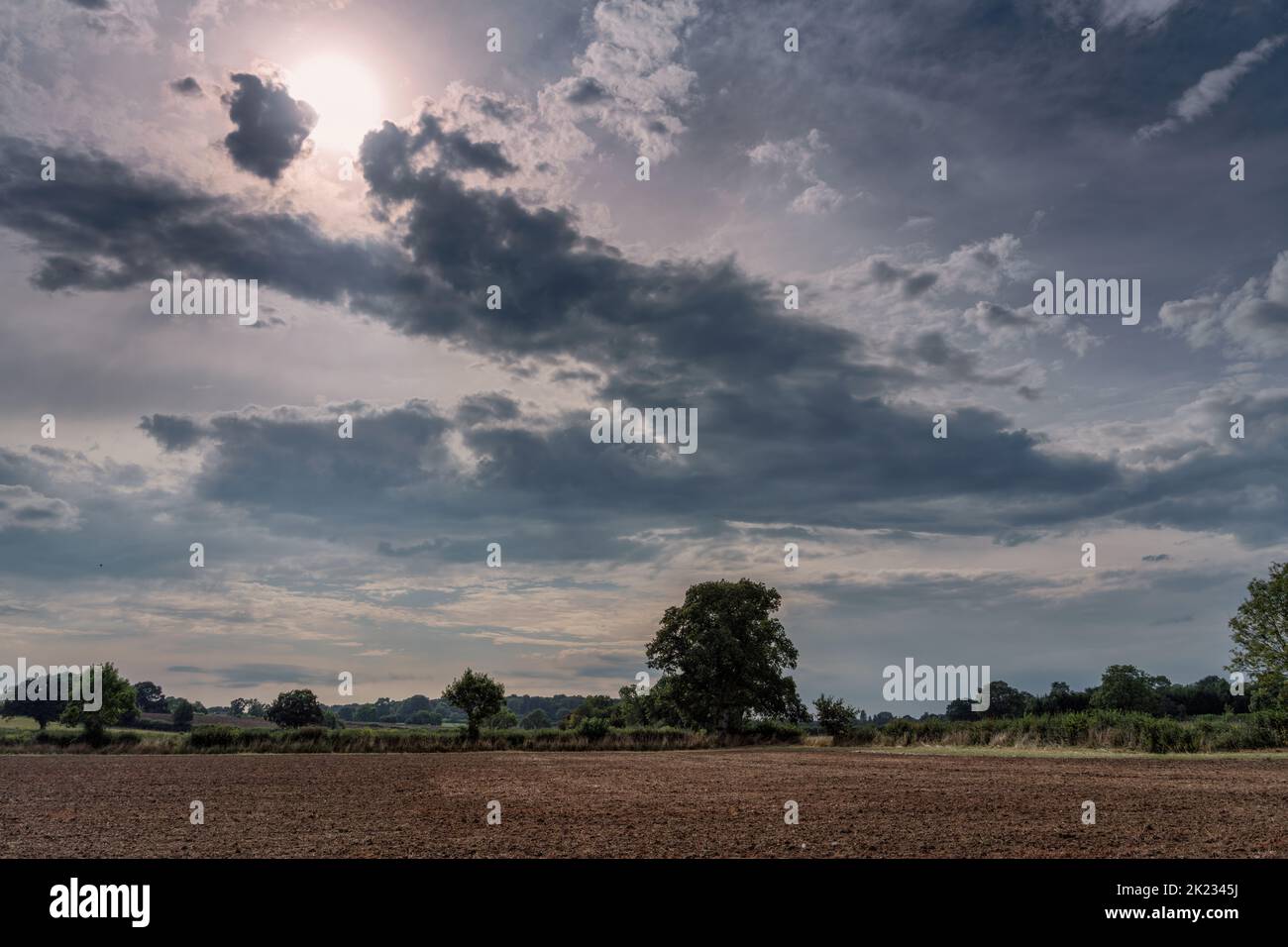 Dramatischer bewölkter Himmel mit Sonne, die durch die Wolken über ein gepflügtes landwirtschaftliches Feld bricht Stockfoto